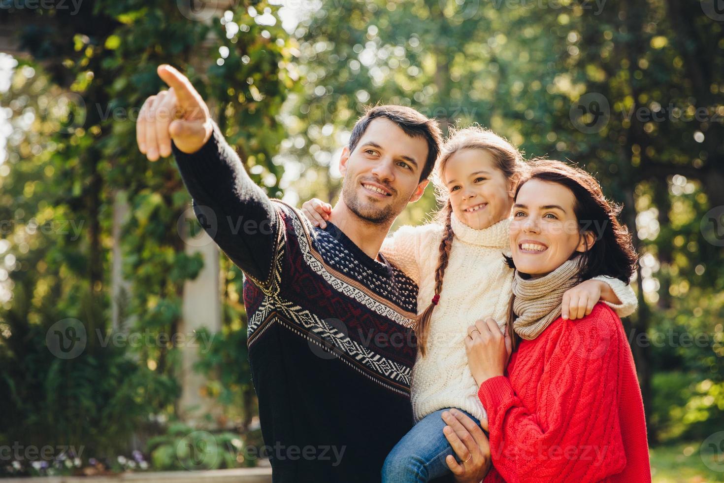 Outdoor portrait of smiling happy friendly family have walk together. Affectionate father shows his small daughter something into distance. Family admire sunrise, beautiful nature, wear warm clothes photo