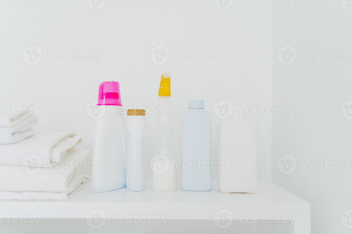 Stack of folded white towels and bottles with detergent against white background. Washing and cleanliness concept. Space for your text photo