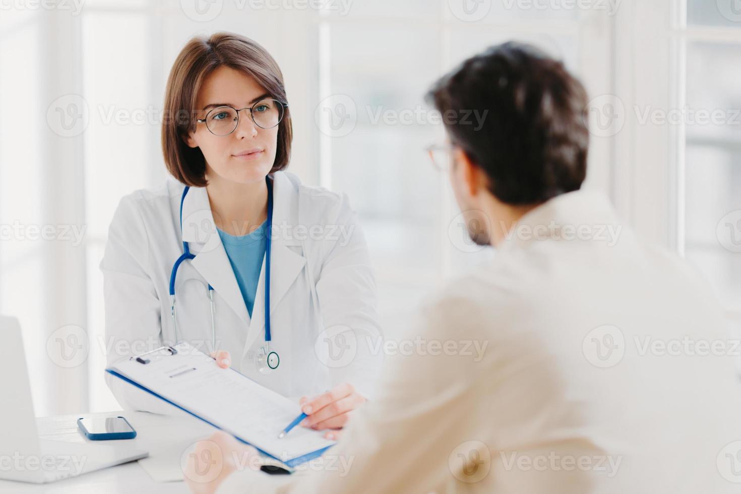 Female general practitioner explains which prescribed medicine patient should buy, gives medical visit consultation. Male clinic visitor tells about health complaints to therapist. Healthcare concept photo