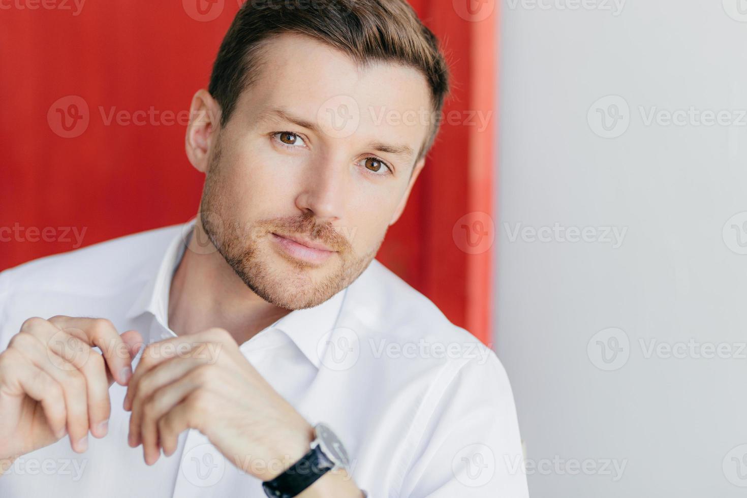 Image of thoughtful self confident male entrepreneur in white shirt, listens attentively his business partner during meeting, poses against white and red background. People, career and lifesyle photo