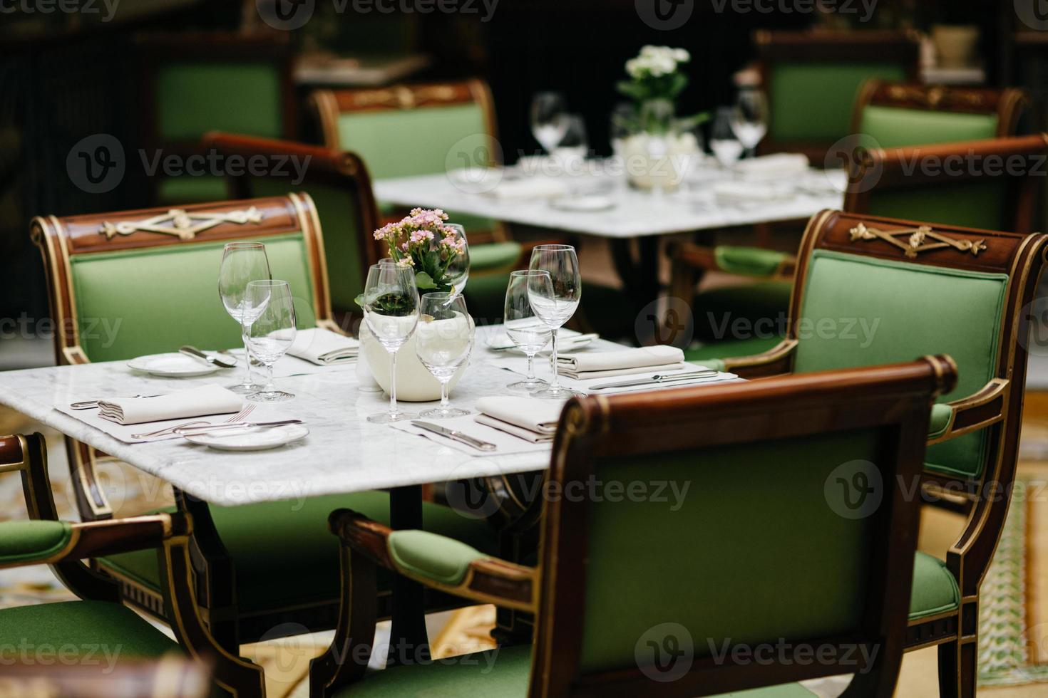 Table served with luxury glasses, cutlery, flowers, green chairs around in cozy restaurant. Nobody in shot. Decorated table for festive event photo