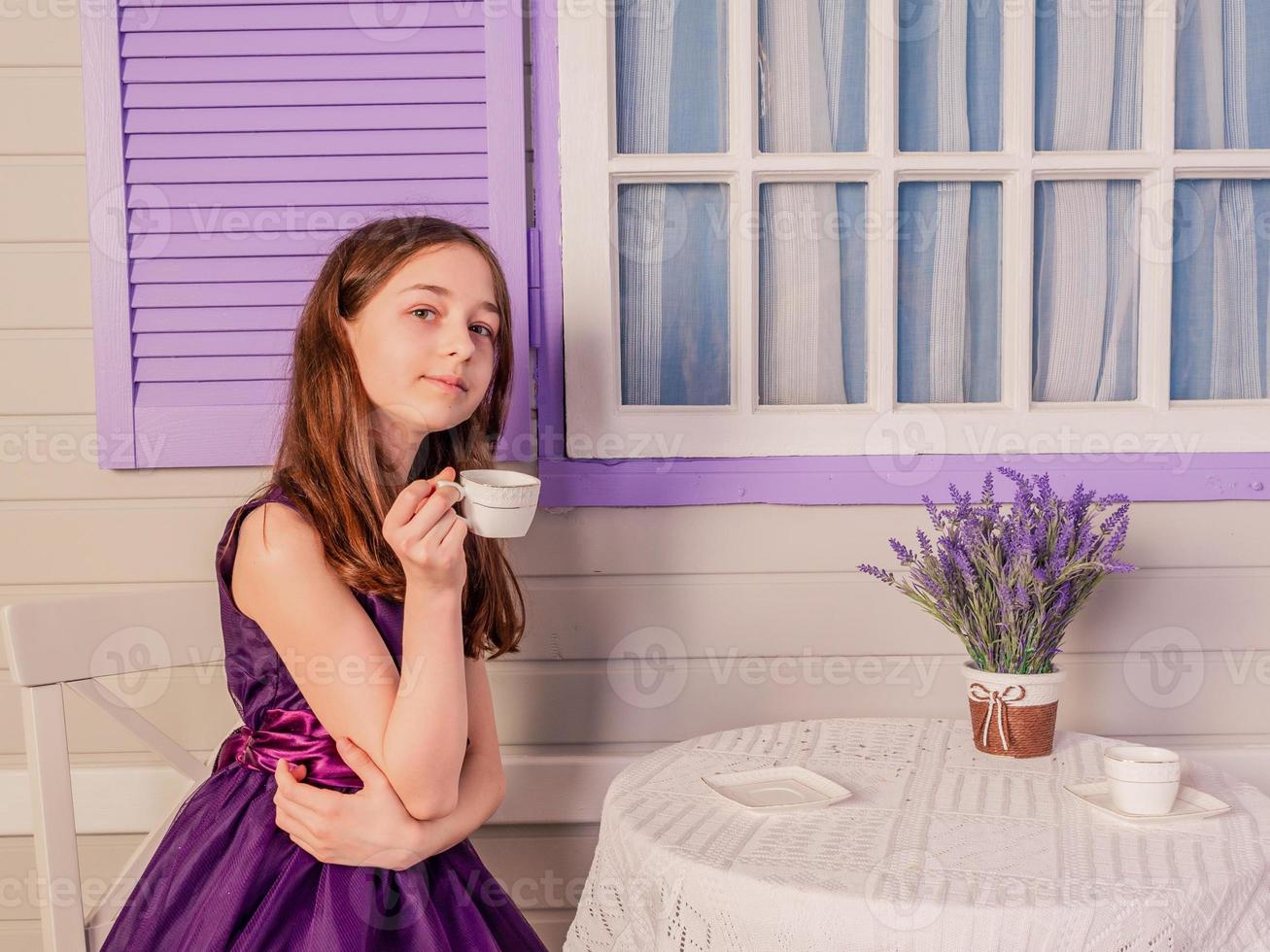 A girl in a purple dress drinks tea while sitting at the table. A teenager at home. photo