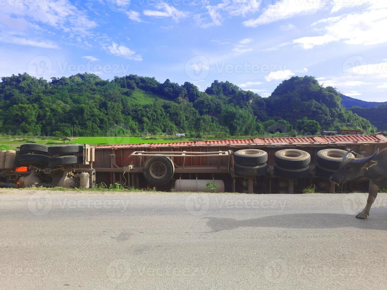Accident truck falls from road to green rice field with mountain and blue sky. photo