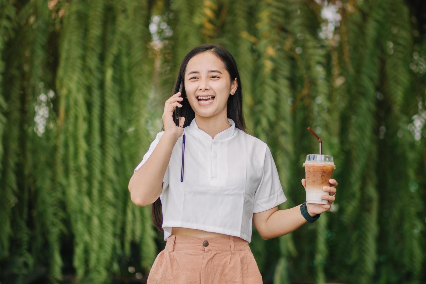 A happy businesswoman in a suit standing in a park and having a phone conversation. She is holding takeaway coffee. A businesswoman in a park on a break photo