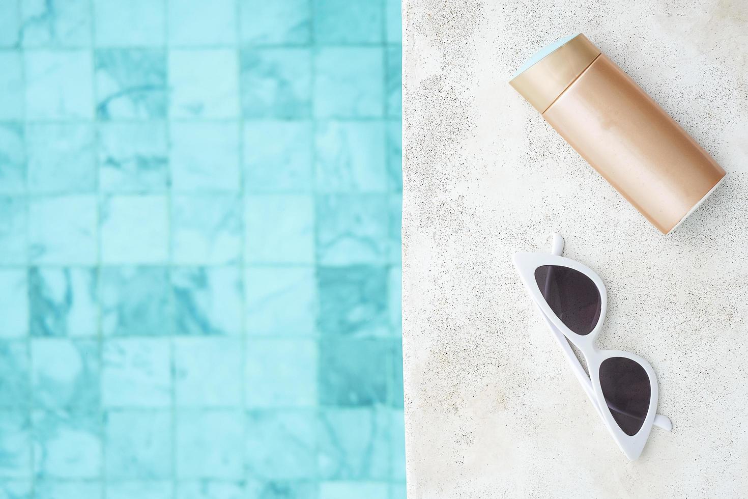 white sunglasses, sunscreen bottle and hat near swimming pool in luxury hotel. Summer travel, vacation, holiday and weekend concept photo