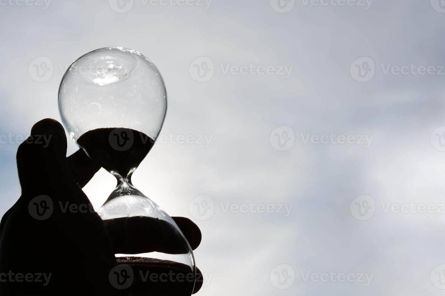 An hourglass in a man's hand against the sky. photo