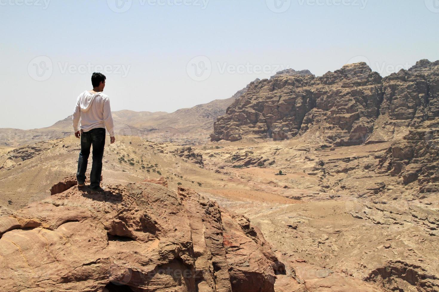 Young man on top of a peak looking over a valley in the rugged landscape of Petra, Jordan photo