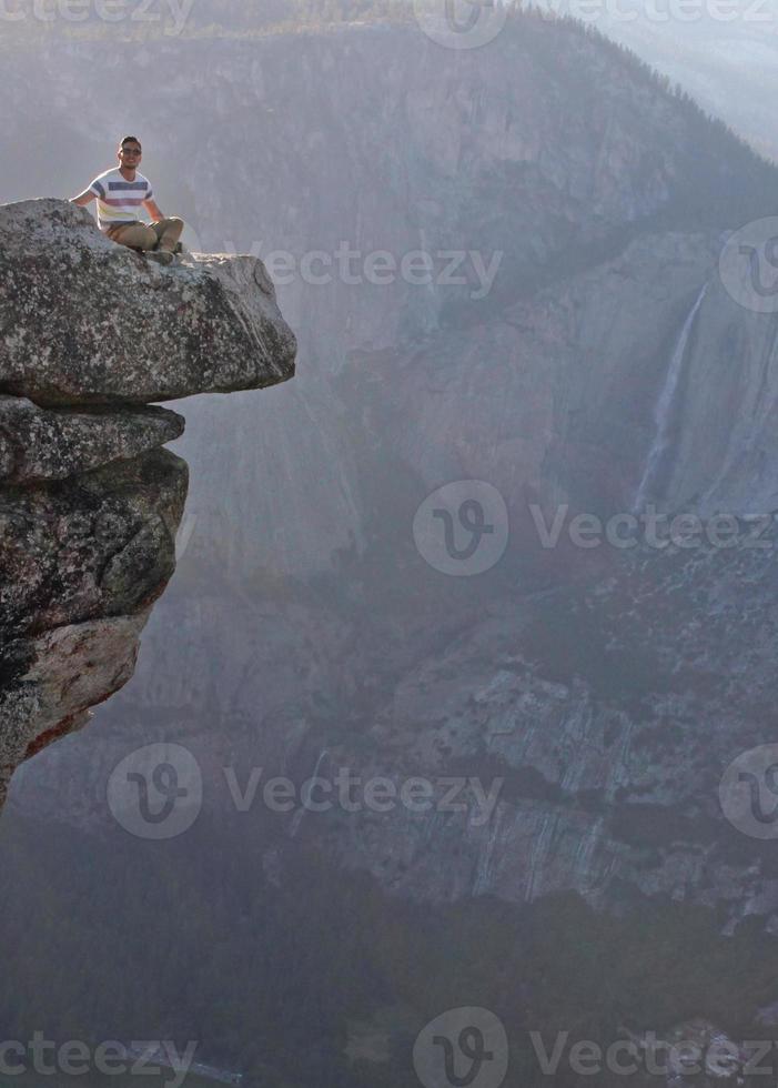 Young man raises his arms at the edge of steep cliffs in Yosemite national park photo