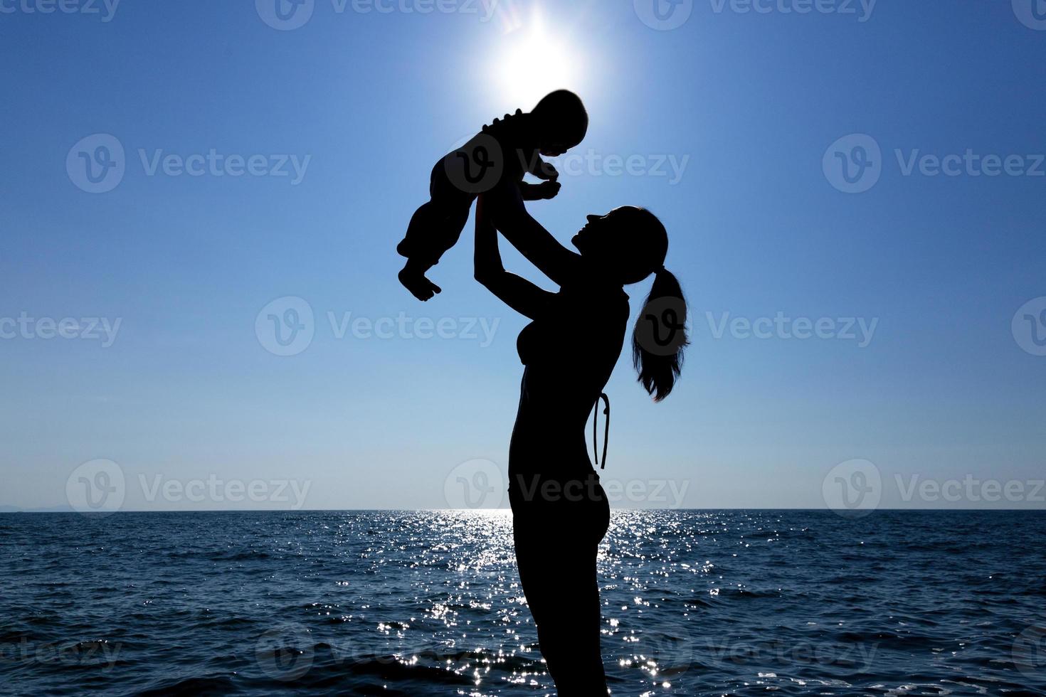 A young girl holds a child in her arms against the sun. Silhouette photography. photo