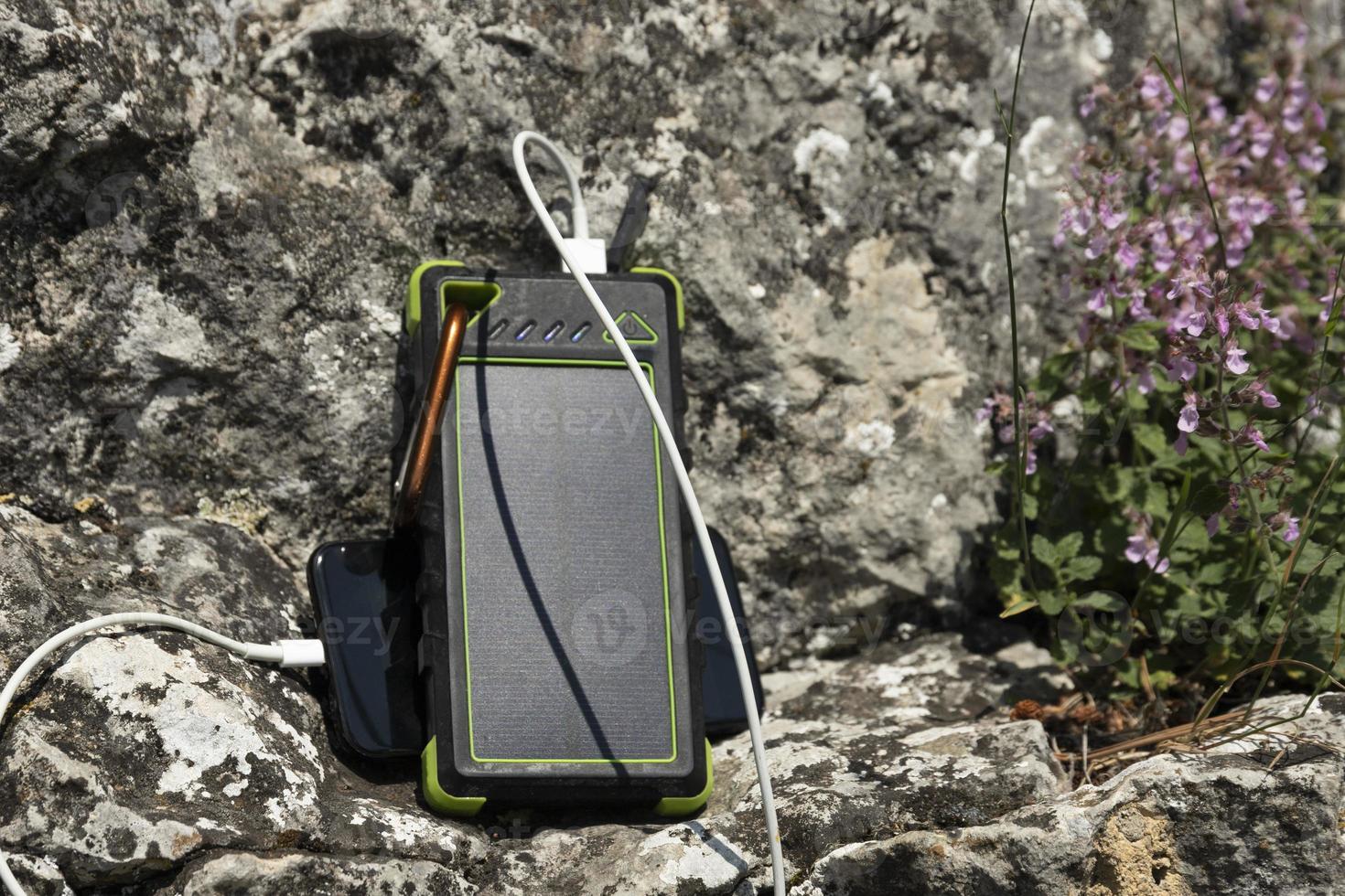 The smartphone is charged with a portable solar power bank charger on a rock during extreme travel. photo