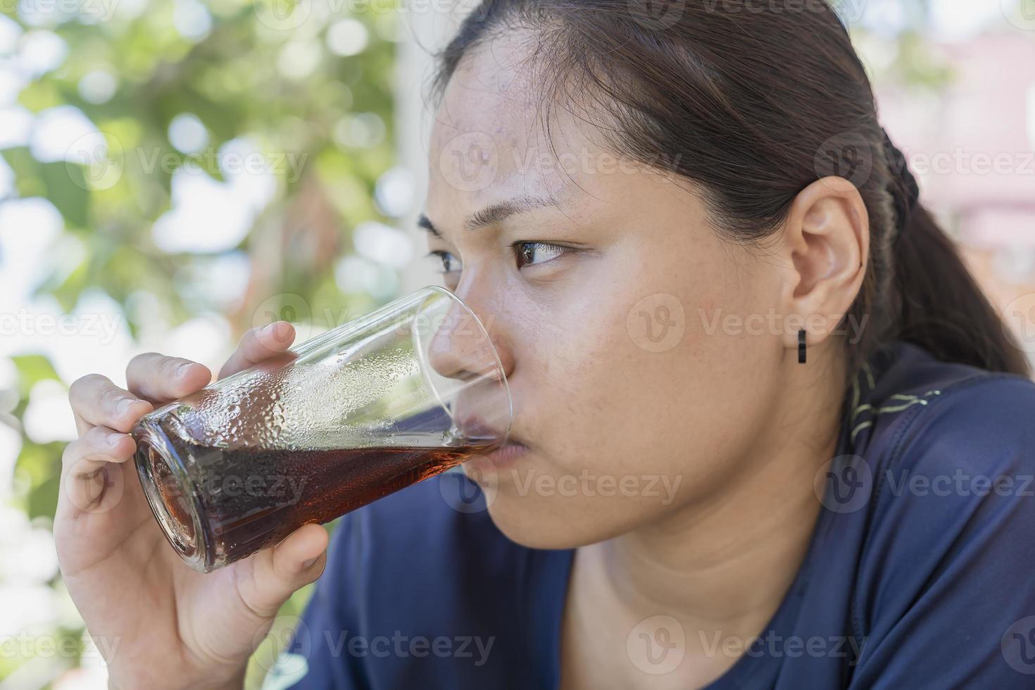 atractiva mujer joven sentada en una silla para tomar refrescos de cola. una mujer disfruta bebiendo coca cola en el café. chica con un vaso de coca cola para relajarse en vacaciones o vacaciones. foto