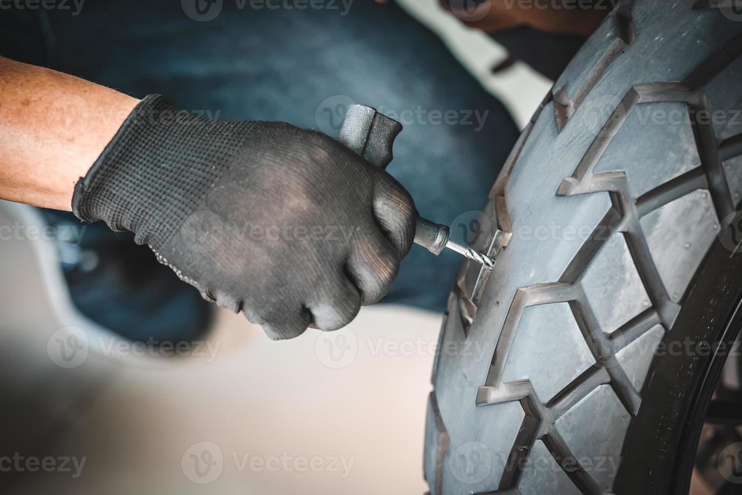 el ciclista usa un kit de tapones para neumáticos y trata de arreglar un agujero en la pared lateral del neumático, repara un neumático plano de motocicleta en el garaje. concepto de mantenimiento y reparación de motocicletas foto