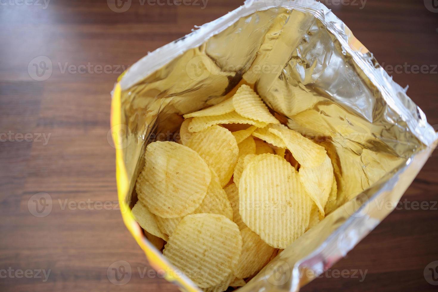 Potato chips in open snack bag close up on table floor photo