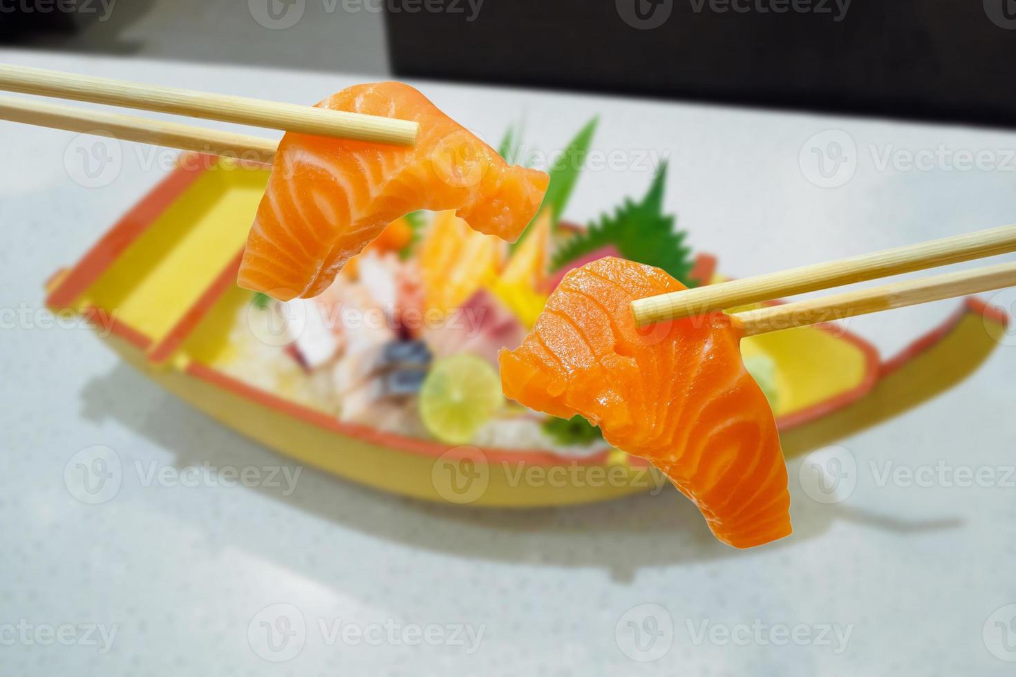 salmon in chopsticks with japanese sashimi set on boat plate photo