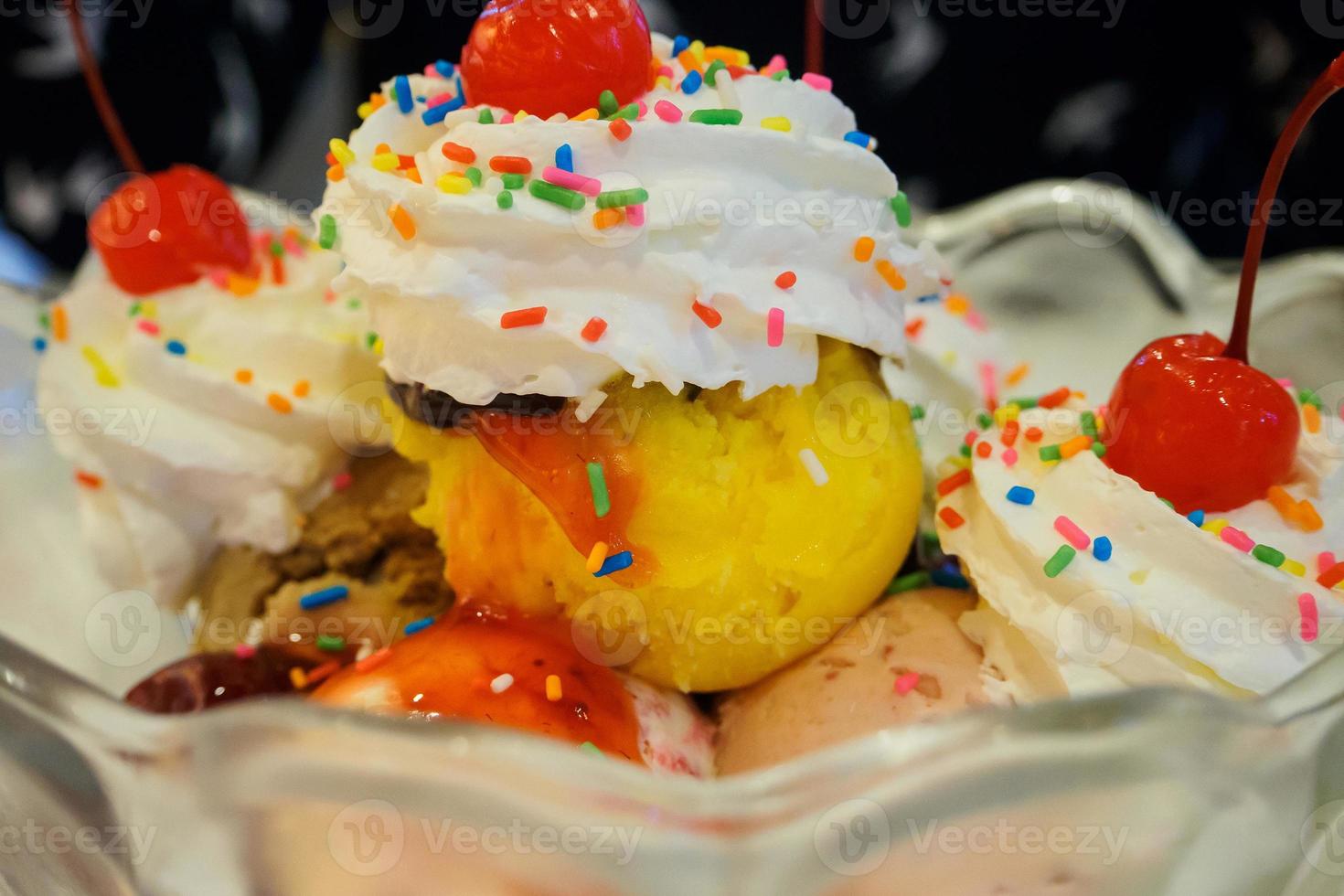 Ice cream sundae scoops with cherry and whipped cream in glass bowl photo