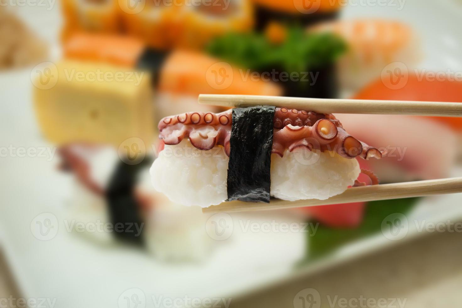 Sushi in chopsticks with blur sushi on a plate background photo