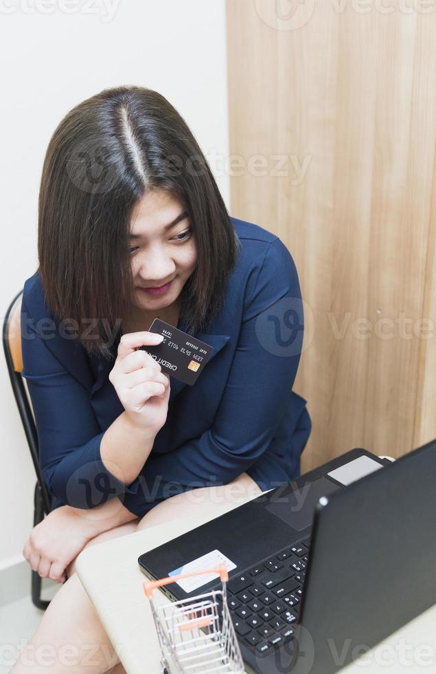 A woman holding a credit card, which is paying online, sits on the chair in the living room at home on a laptop. The concept of online shopping. photo