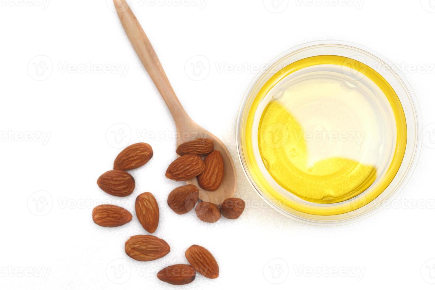 Yellow almond oil in a clear bowl with a wooden spoon next to it and several almonds on a white background.top view,top-down.flat lay. photo