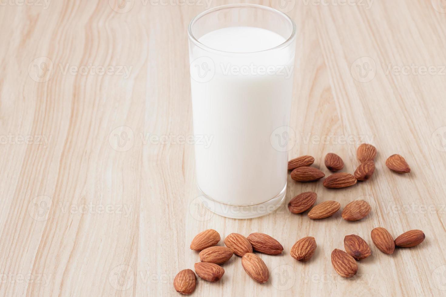 almond milk in glass on wood background with nuts around the bowl.selective focus.front view.copy space. photo