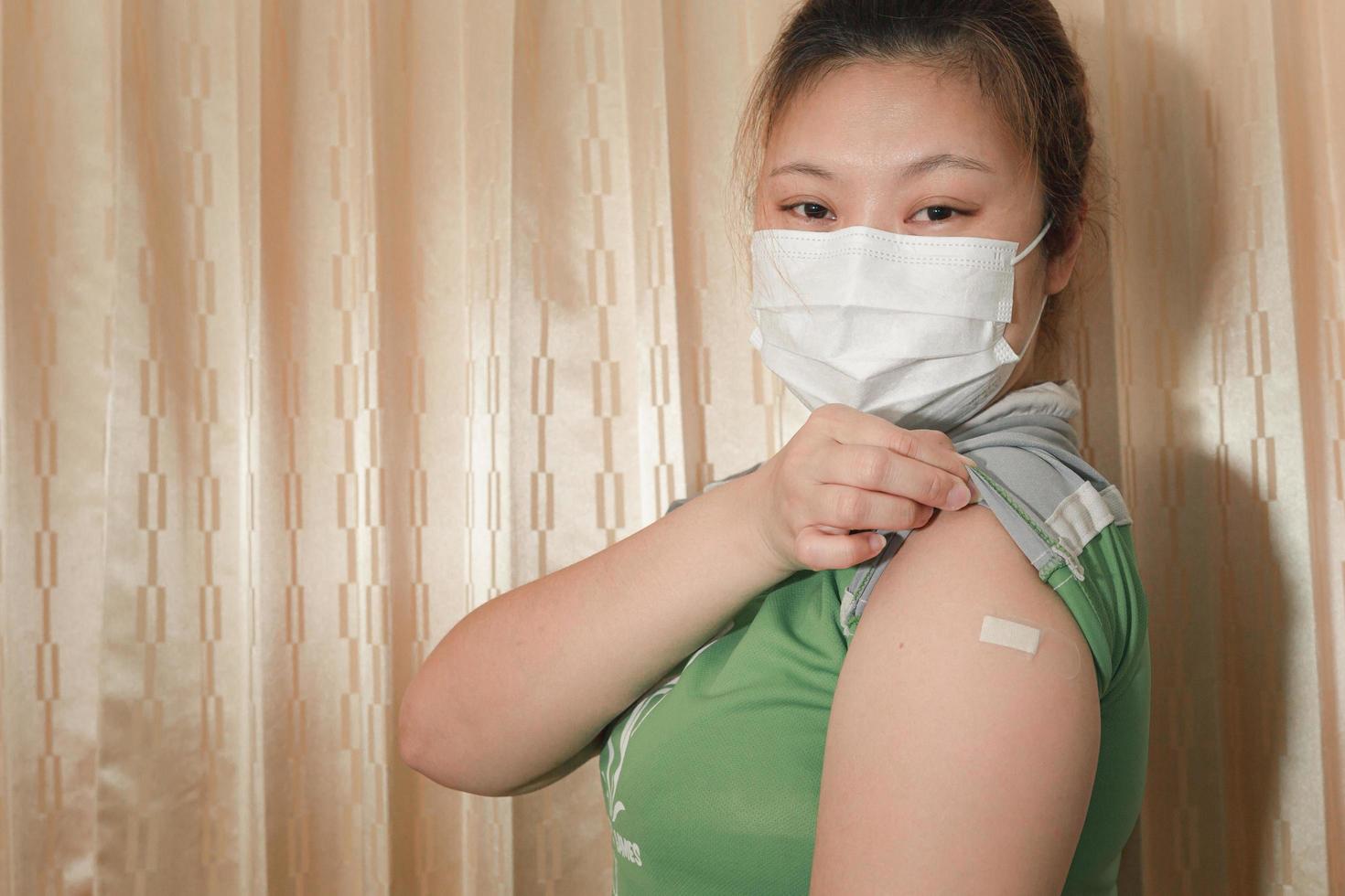 Asian woman wearing a mask, showing plaster on her arm after vaccination against COVID-19, coronavirus vaccination concept. photo