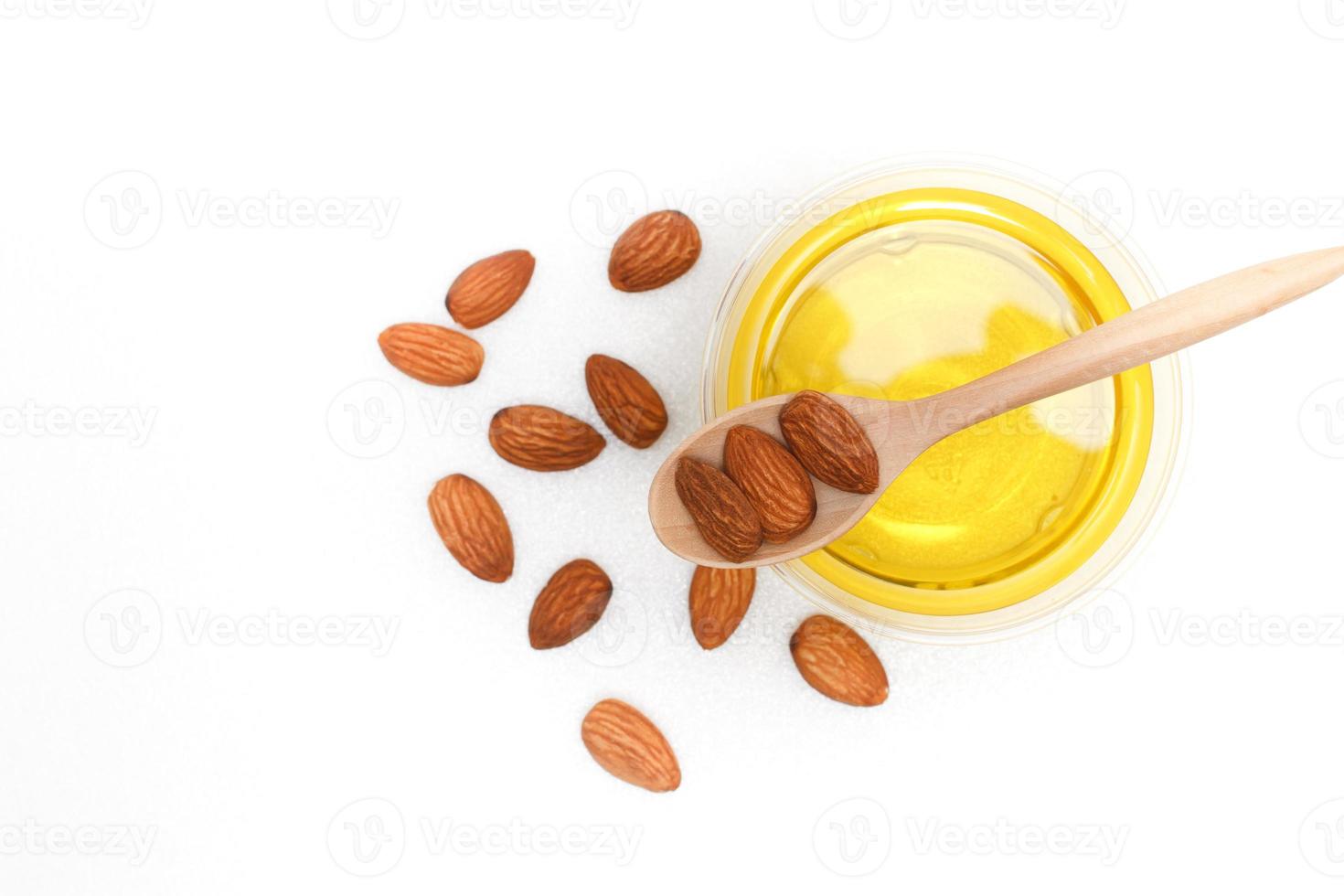 Yellow almond oil in a clear bowl with a wooden spoon next to it and several almonds on a white background.top view,top-down.flat lay. photo