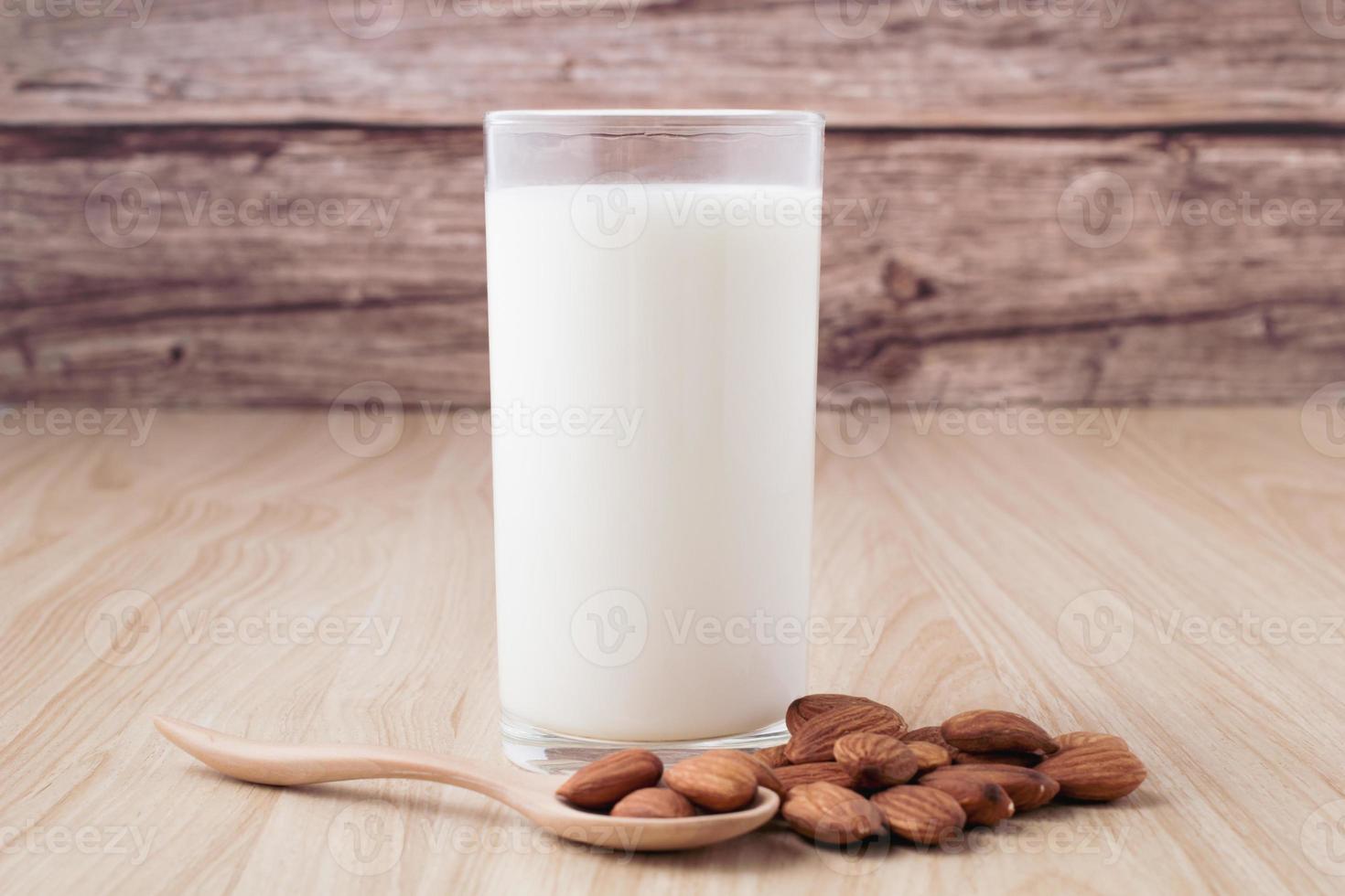 almond milk in glass on wood background with nuts around the bowl. photo