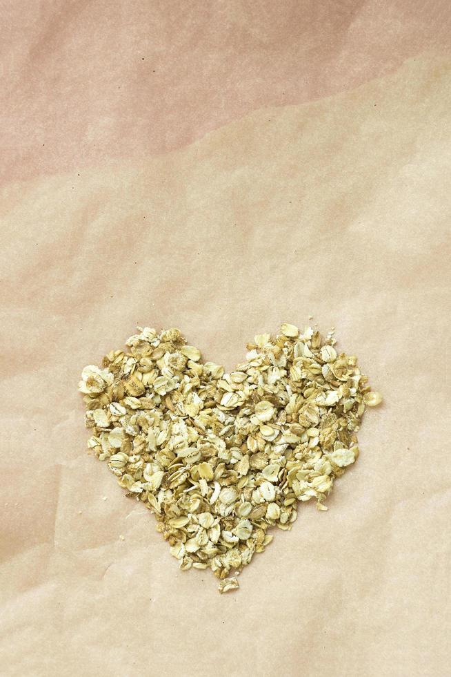 Oatmeal flakes in shape of heart on brown kraft paper. Concept of diet and healthy eating. Closeup vertical image in top view with copy space. photo