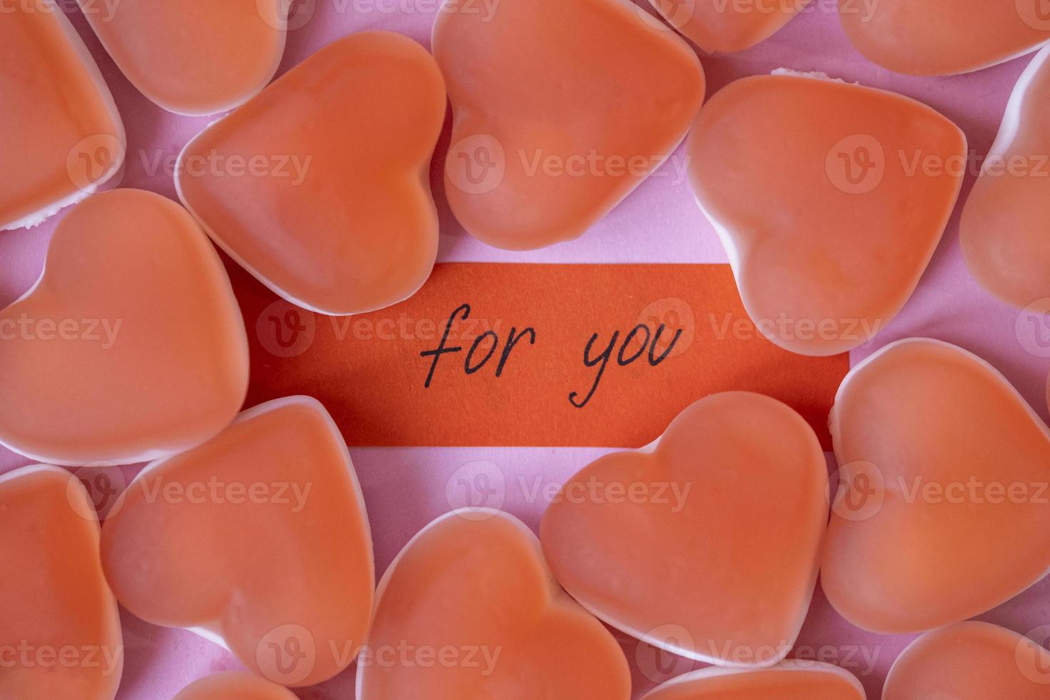 Red candy marmalade in shape of heart with a note FOR YOU on pink background. Sugar gummy candy. Valentine's Day concept. Geometric pattern. Minimal design, flat lay, top view. photo