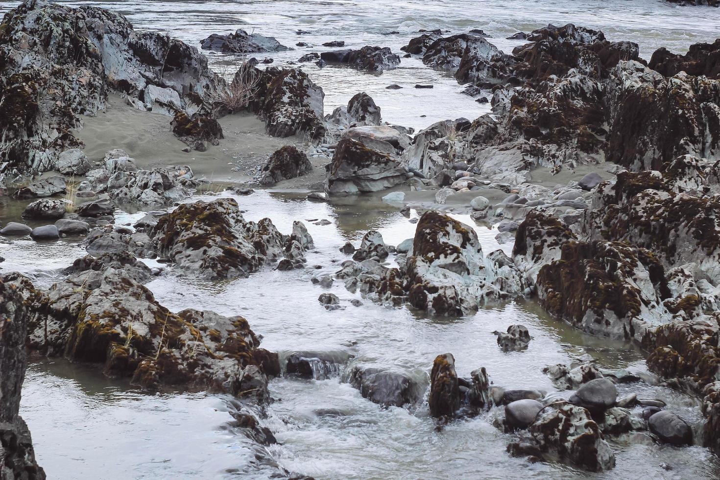 Small river flows on stones with moss. Closeup water and rock. Cloudy day, nature photo