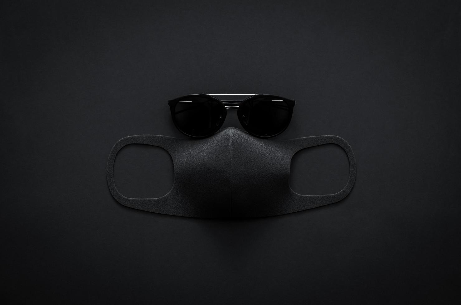 Sunglasses and face mask on dark background for minimalist flat lay black concept photo