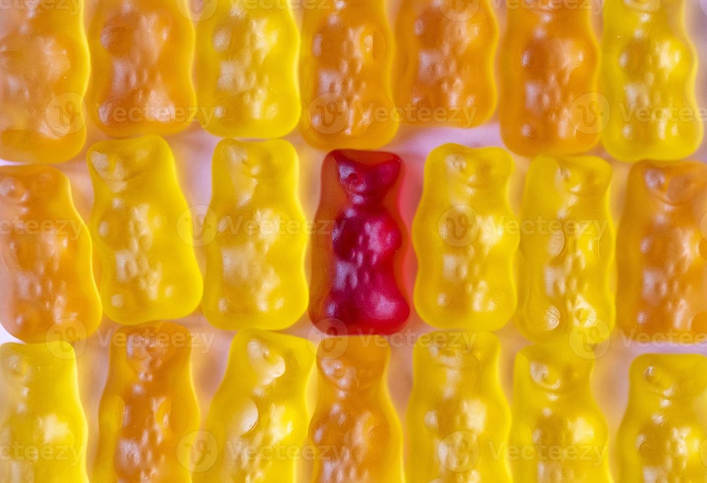Unique red gummy bear and group of many yellow bears. Standing out from crowd, individuality and difference concept. Minimal design, flat lay, top view. photo