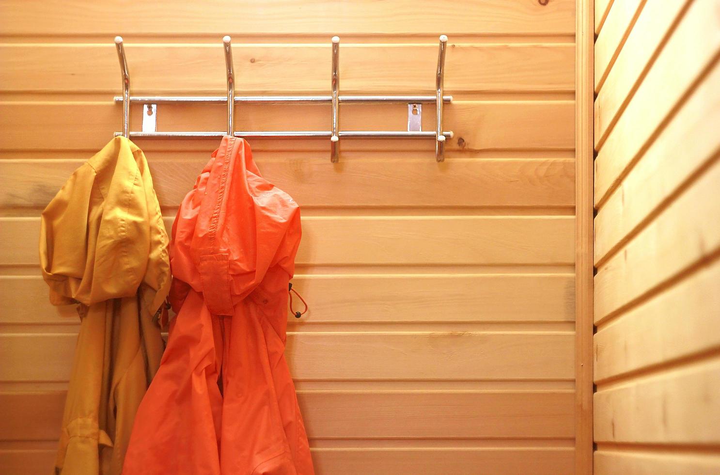 Red and yellow raincoats hang on hanger on wooden wall. Outerwear in hallway. Protective clothing against rain and wind photo