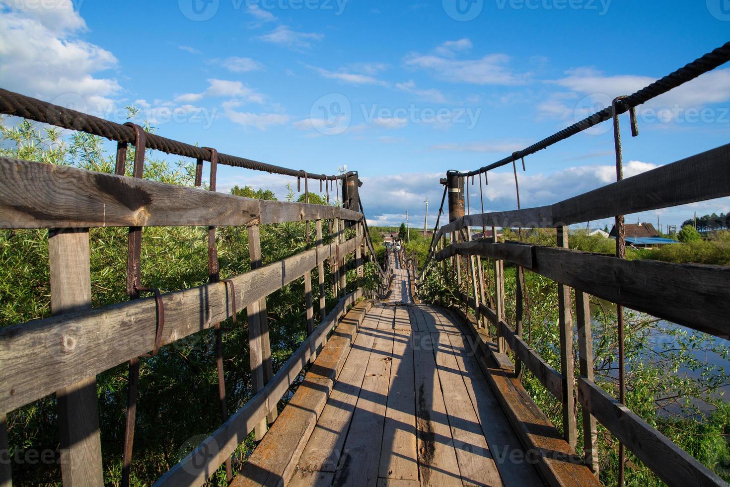 puente de madera con bisagras que cruza el río hacia el bosque. foto