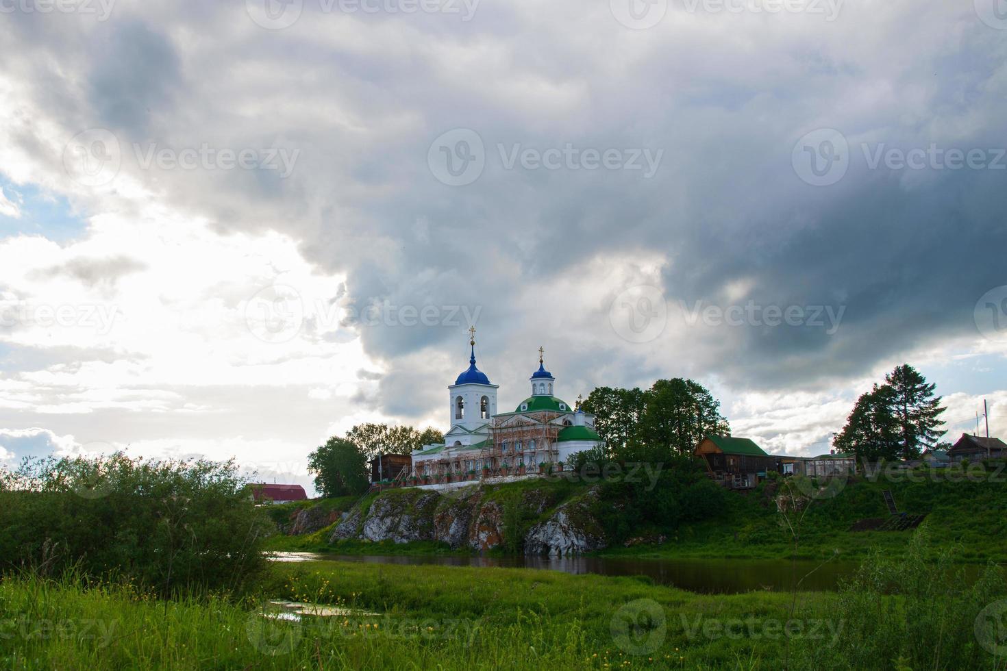 a village on the river bank with bright green grass and a beautiful sky. photo