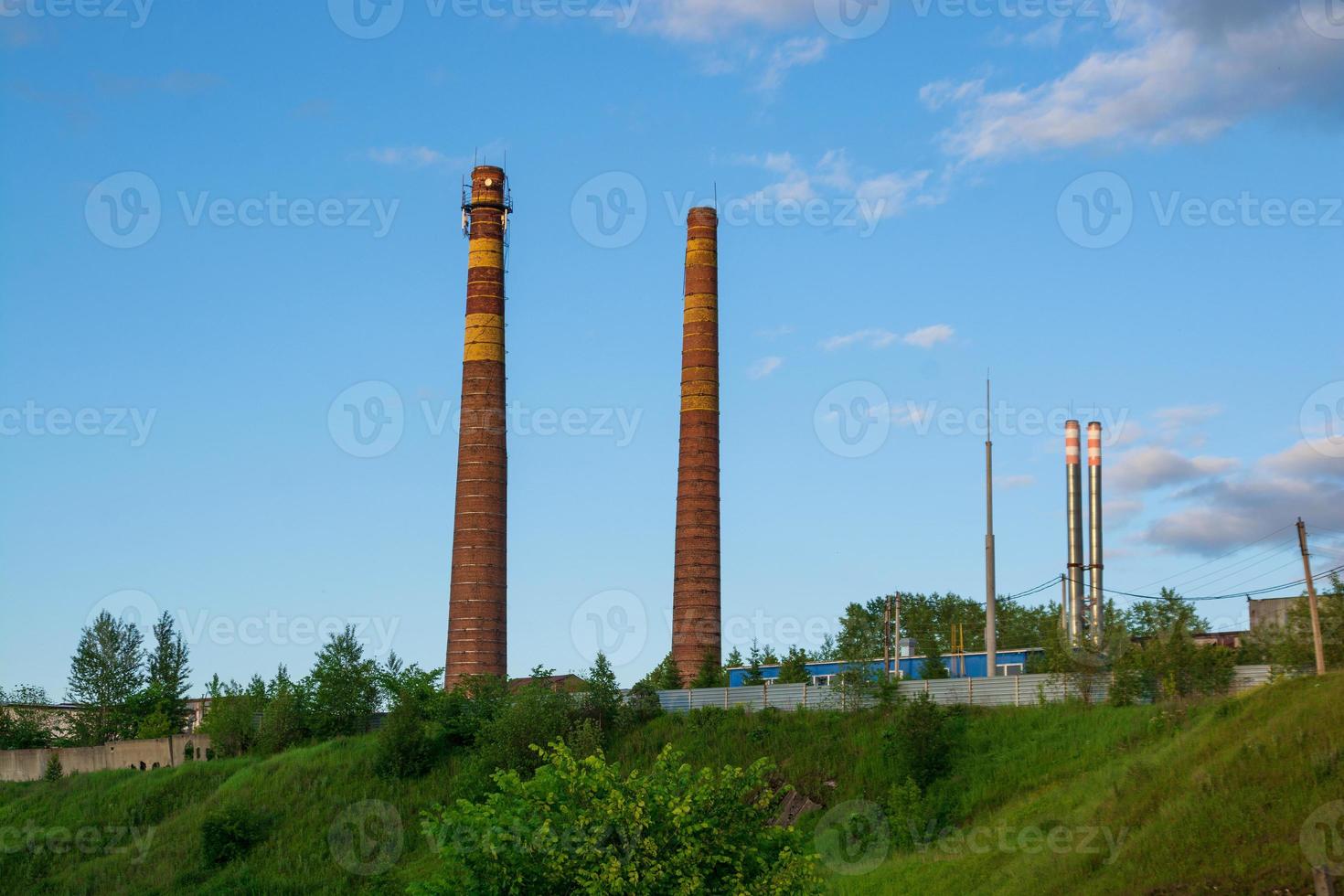 factory pipes on the background of green grass and blue sky with clouds. photo