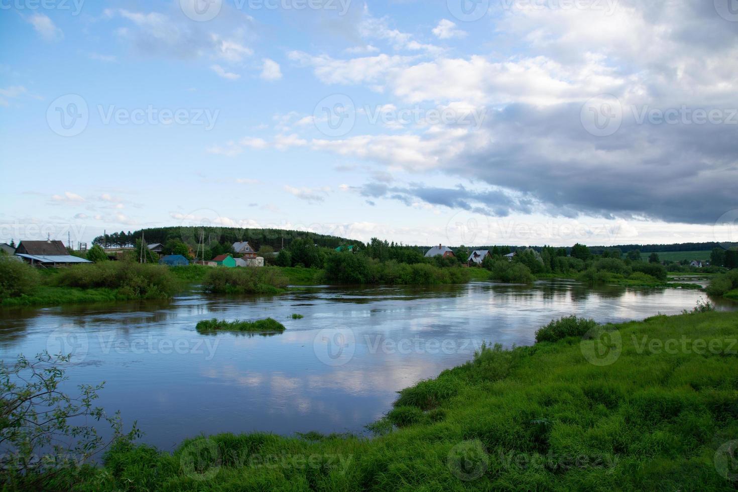 un pueblo en la orilla del río con hierba verde brillante y un hermoso cielo. foto