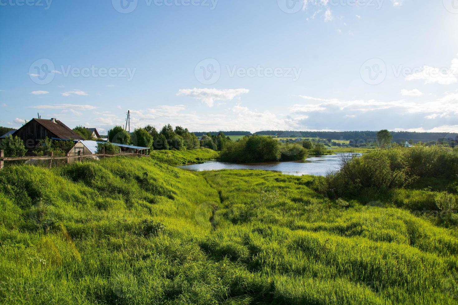 a village on the river bank with bright green grass and a beautiful sky. photo