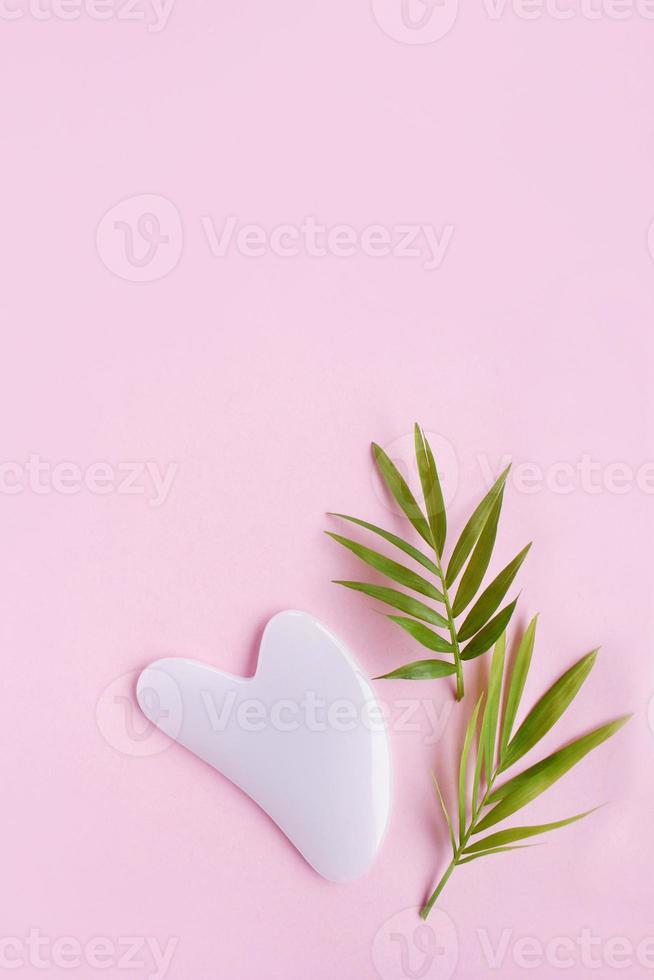 Top view of pink heart shaped guasha stone made of quartz crystal on pink background with copy space. Concept of alternative skin care treatment, self massage and acupressure photo