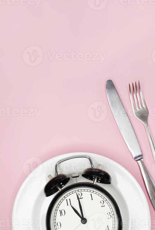 concepto de ayuno intermitente, dieta cetogénica, pérdida de peso. tenedor y cuchillo, despertador en placa foto