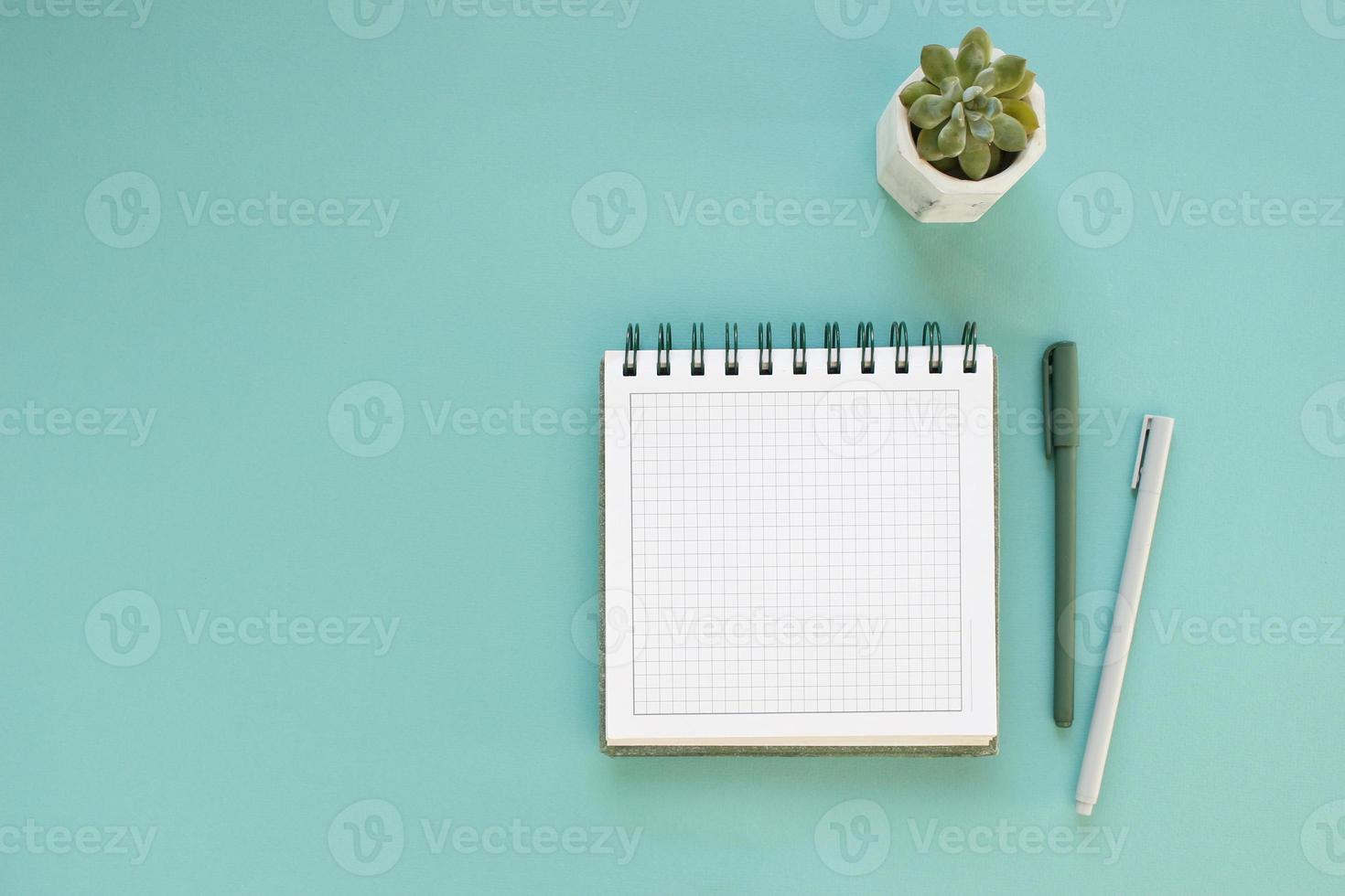 Top view of workspace and opened notebook with mock up blank pages on blue background. Flat lay photo