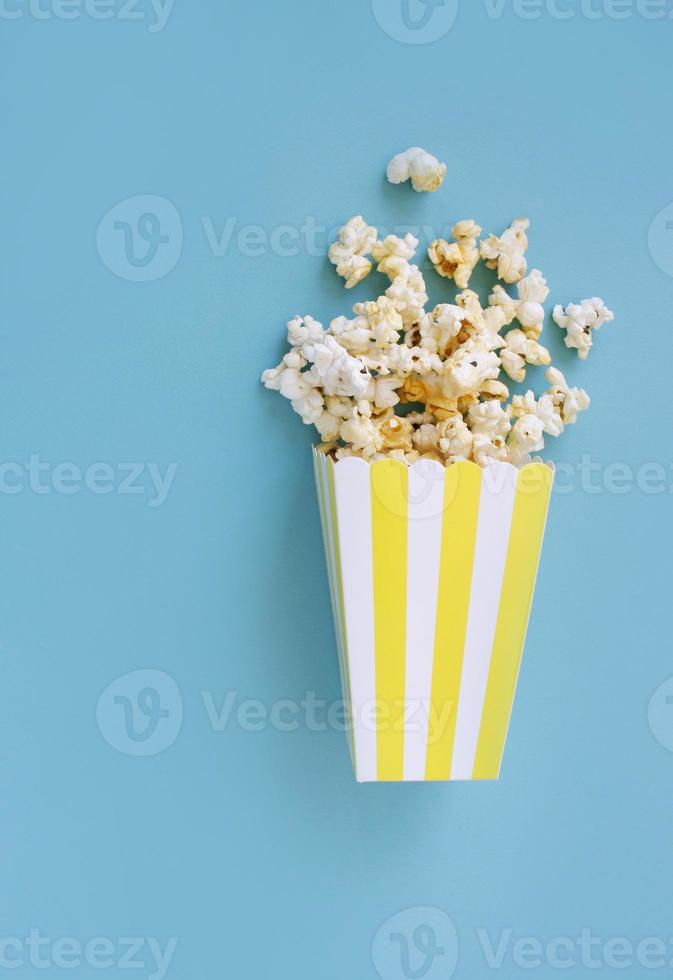 Spilled popcorn and paper bucket on blue background. Movie night concept. Copy space for text photo