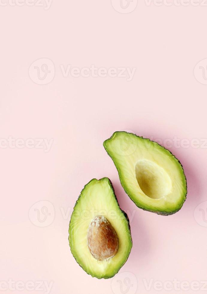 endecha plana de un aguacate fresco a la mitad sobre un fondo rosa mínimo. alimentos naturales crudos. foto