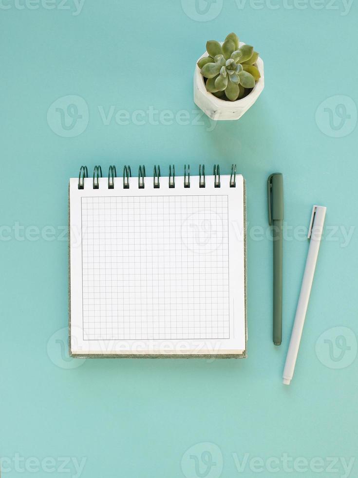 Top view of workspace and opened notebook with mock up blank pages on blue background. Flat lay photo