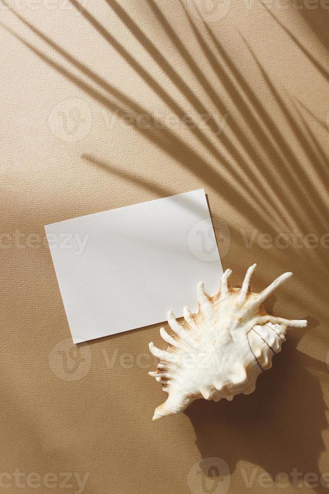 Card mockup with copy space top view, flat lay. Greetings, wedding invitations blank, paper sheet and dry palm leaf on beige background. photo
