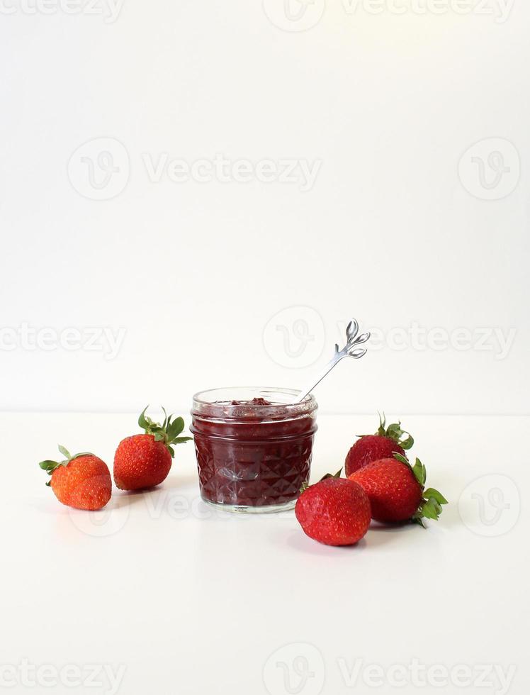 Homemade strawberry preserves or jam in a mason jar surrounded by fresh organic strawberries. Selective focus with white background. photo