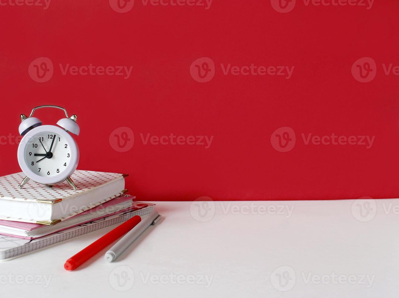 Creative desk with notebook, desk objects, office supplies, books, on white table, red wall. Student's desk. Creative workspace front view. Mock up photo