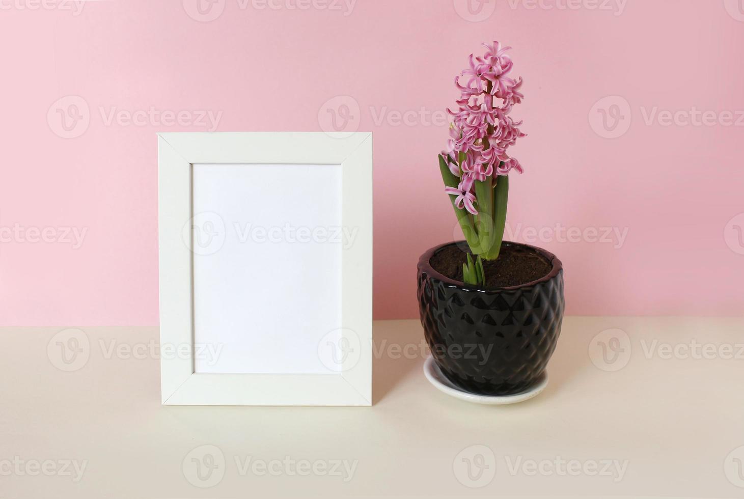 photo frame with white blank card and flowers on pastel pink background. Mock up poster frame. Stylish template.