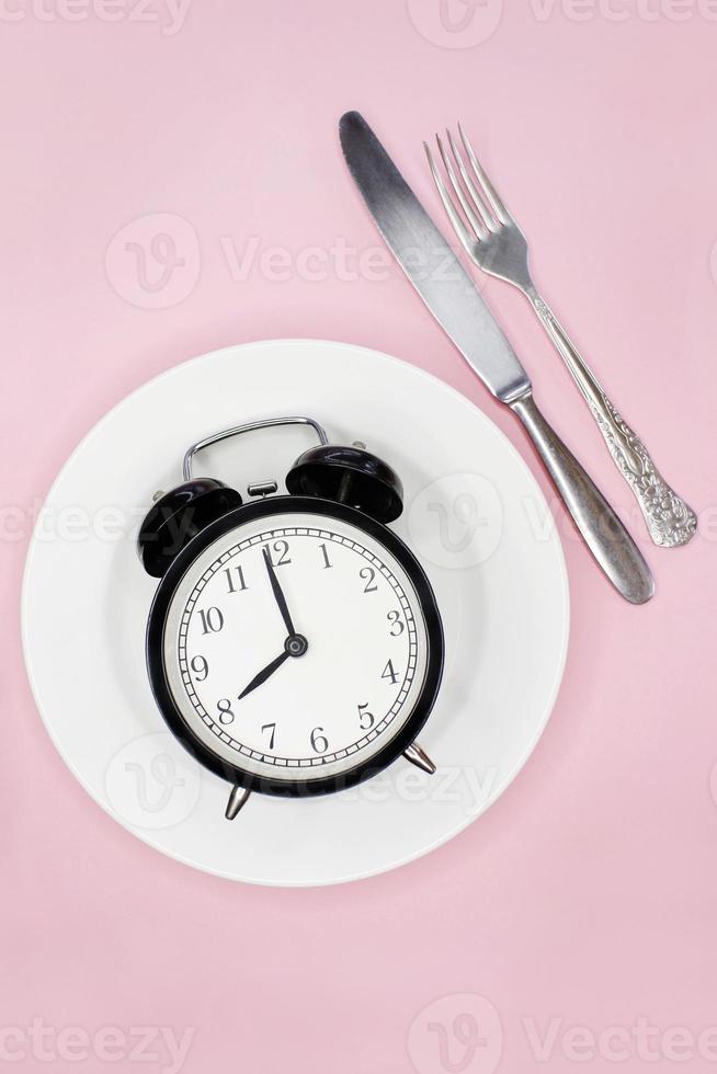 concepto de ayuno intermitente, dieta cetogénica, pérdida de peso. tenedor y cuchillo, despertador en placa foto