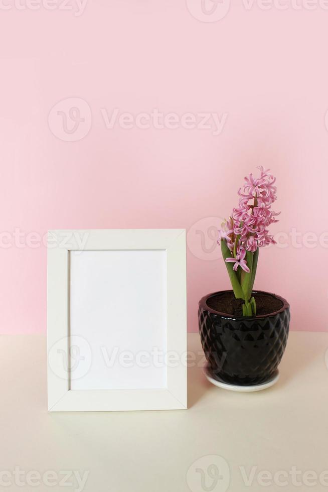 photo frame with white blank card and flowers on pastel pink background. Mock up poster frame. Stylish template.