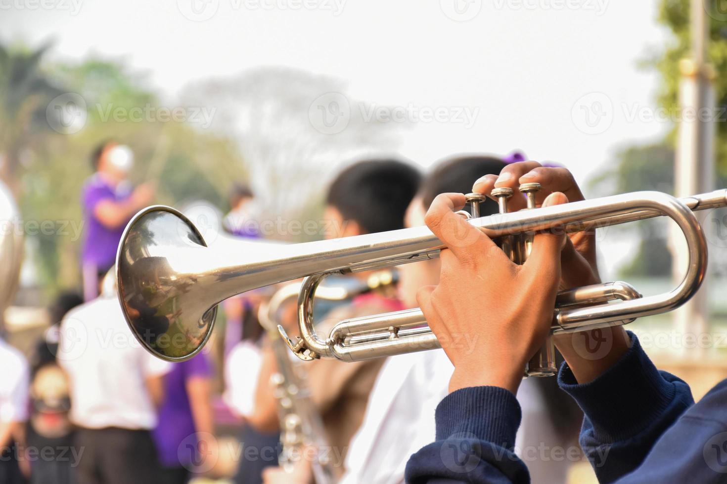 Asian young boy student blowing a trumpet with school marching band, blurred background photo